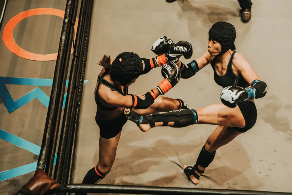 Two women fighting with shin guards in a ring